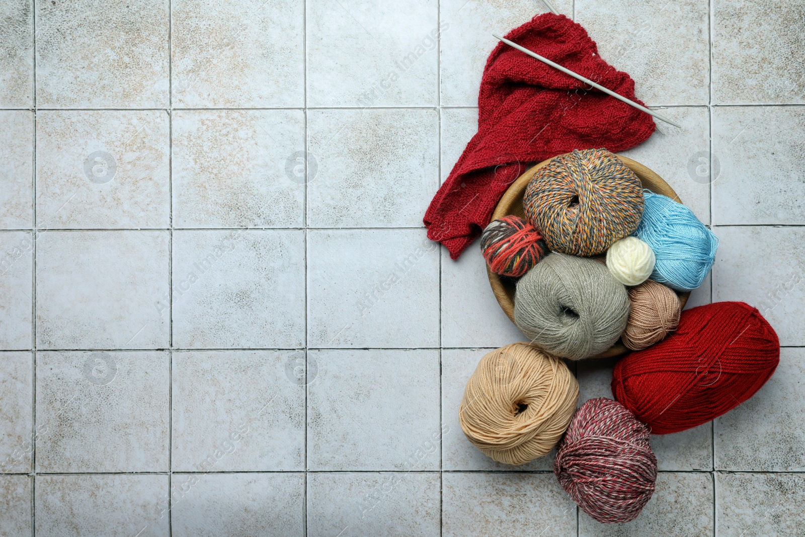 Photo of Soft woolen yarns, knitting and needles on grey tiled background, flat lay. Space for text