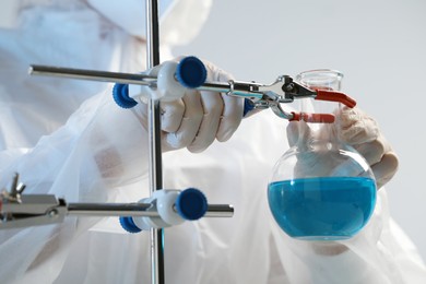 Photo of Scientist working with flask of light blue liquid on grey background, closeup