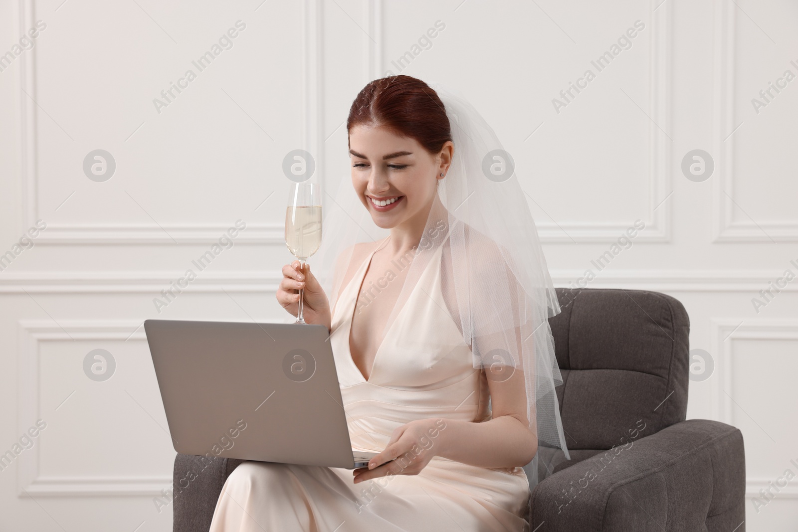 Photo of Happy bride with glass of sparkling wine and laptop indoors