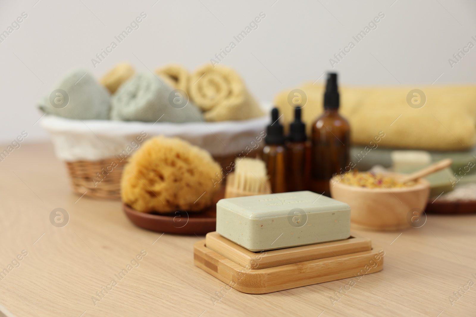 Photo of Soap bar, sponge and bottles of essential oils on light wooden table. Spa therapy