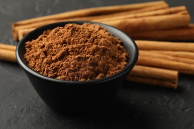 Photo of Aromatic cinnamon powder and sticks on black table, closeup