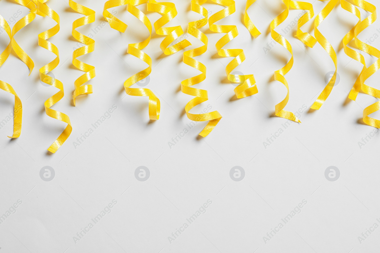 Photo of Yellow serpentine streamers on white background, top view