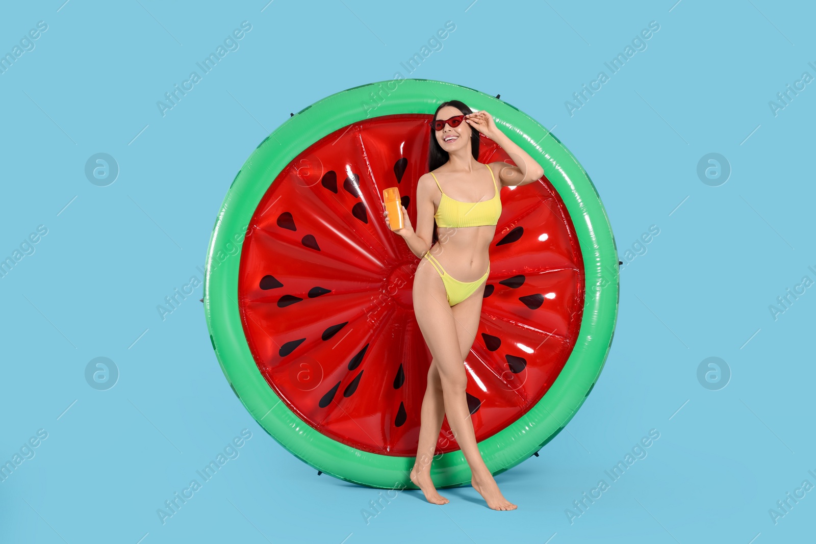 Photo of Young woman with sun protection cream near inflatable mattress against light blue background