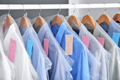 Photo of Rack with clean clothes on hangers after dry-cleaning indoors