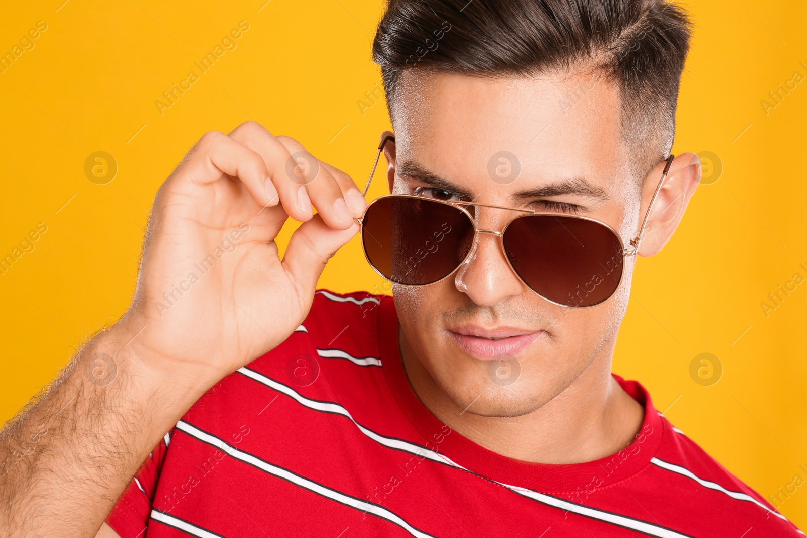 Photo of Handsome man wearing sunglasses on yellow background, closeup