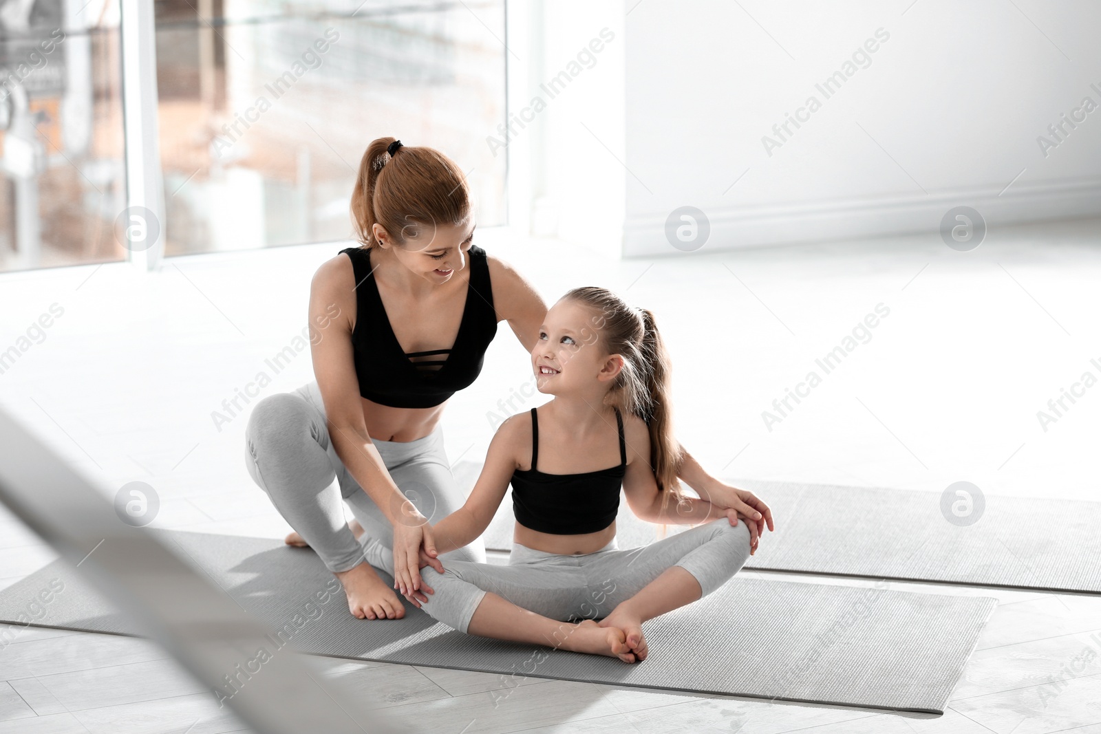 Photo of Mother and daughter in matching sportswear doing yoga together at home