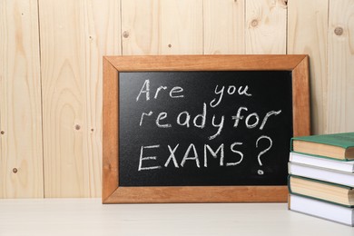 Blackboard with question Are You Ready For Exams? on white table near wooden wall