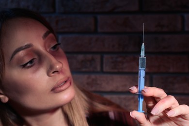 Photo of Drug addicted woman with syringe near brick wall, focus on hand