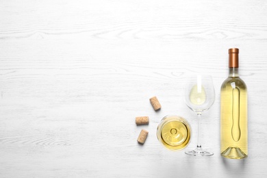 Photo of Glasses and bottle with white wine on wooden background, flat lay. Space for text