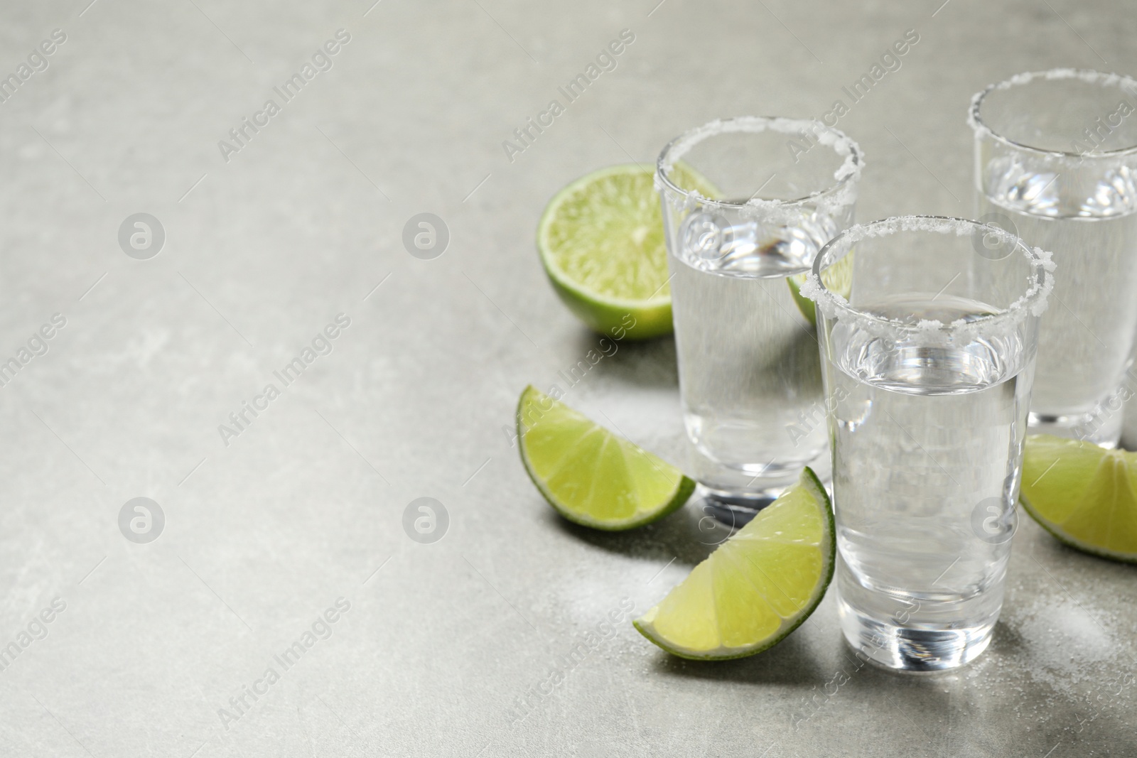 Photo of Mexican Tequila shots with salt and lime slices on grey table. Space for text