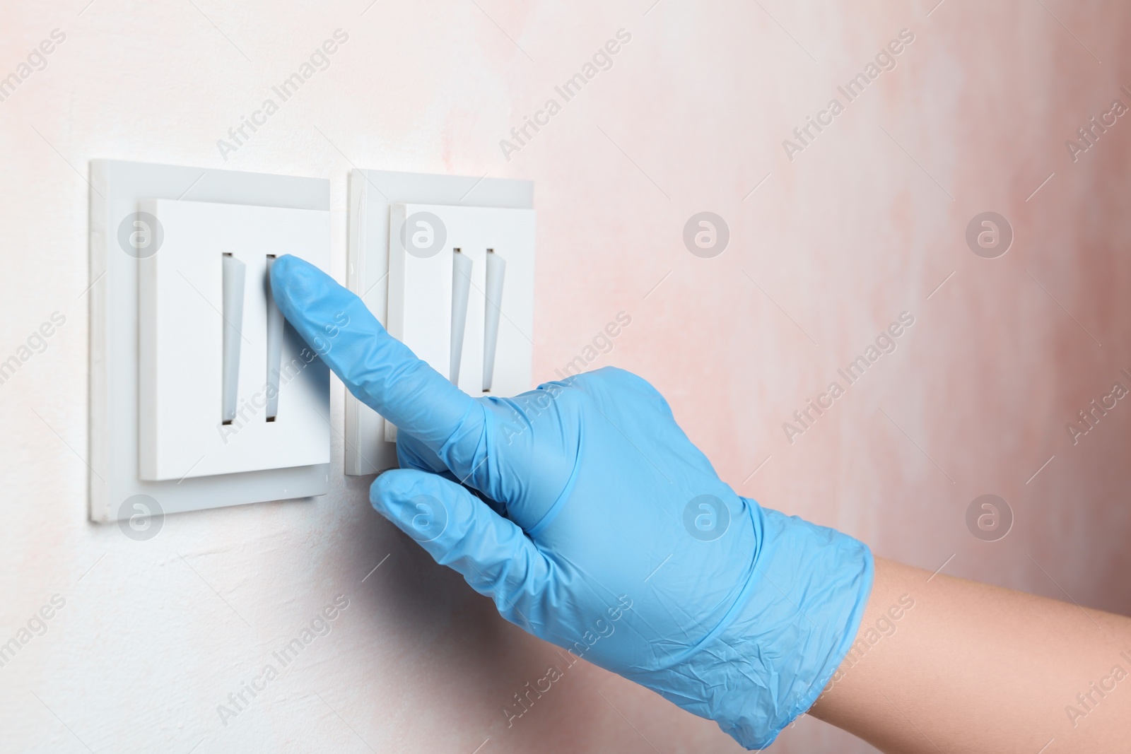 Photo of Woman in protective gloves pressing button of light switch indoors, closeup