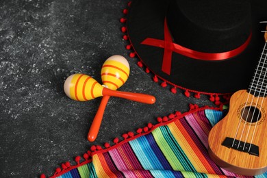 Black Flamenco hat, ukulele, poncho and maracas on dark textured table, flat lay