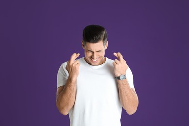 Photo of Man with crossed fingers on purple background. Superstition concept