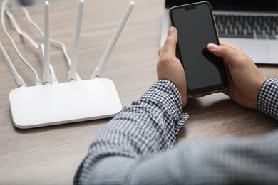 Photo of Man with smartphone and laptop connecting to internet via Wi-Fi router at wooden table, closeup