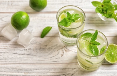 Refreshing beverage with mint and lime in glasses on wooden background