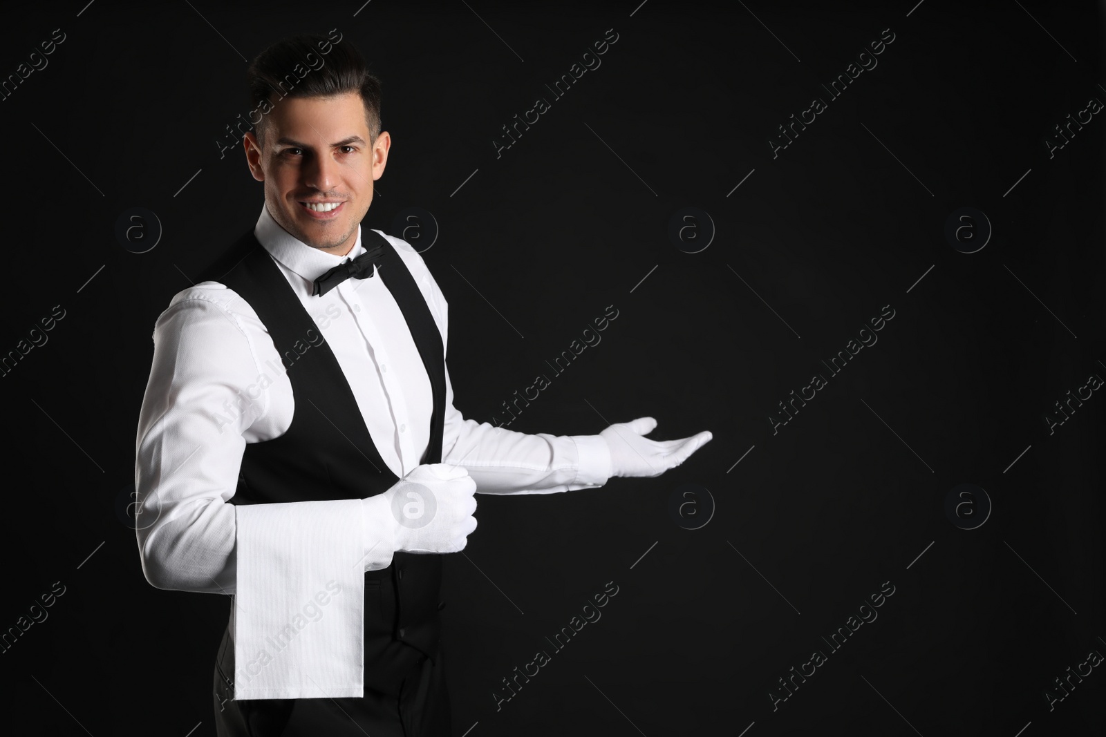 Photo of Handsome butler with towel on black background, space for text