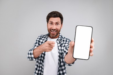 Photo of Handsome man showing smartphone in hand and pointing at it on light grey background