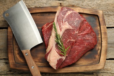 Photo of Fresh raw beef cut, rosemary and butcher knife on wooden table, top view