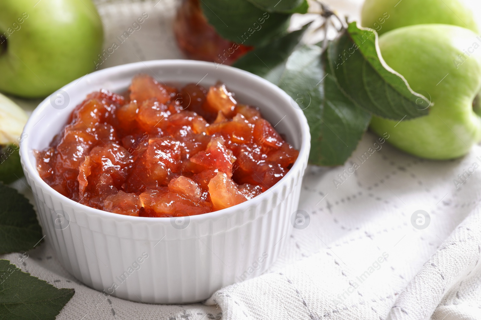 Photo of Bowl of delicious apple jam and fresh fruits on white tablecloth, closeup