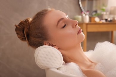 Photo of Young woman using pillow while enjoying bubble bath indoors