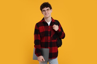 Portrait of student with backpack, laptop and glasses on orange background