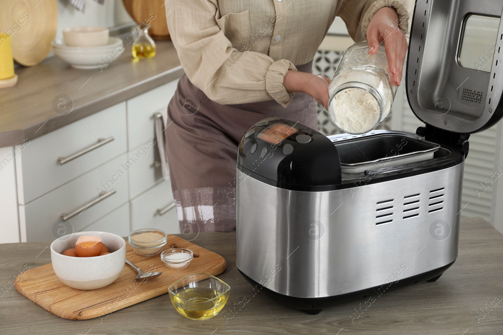 Photo of Making dough. Woman adding flour into breadmaker machine at wooden table, closeup