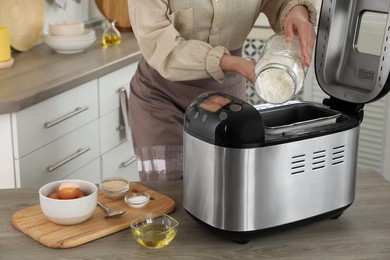 Photo of Making dough. Woman adding flour into breadmaker machine at wooden table, closeup