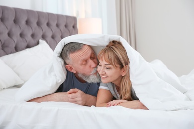 Photo of Mature couple together under blanket in bed at home