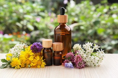 Photo of Bottles of essential oil and different flowers on white wooden table outdoors