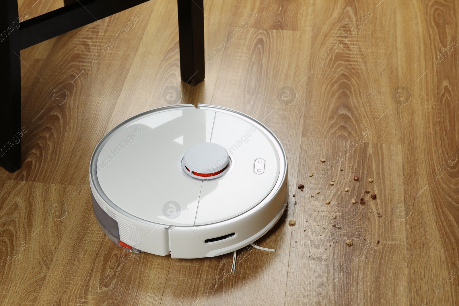 Photo of Robotic vacuum cleaner removing dirt from wooden floor indoors