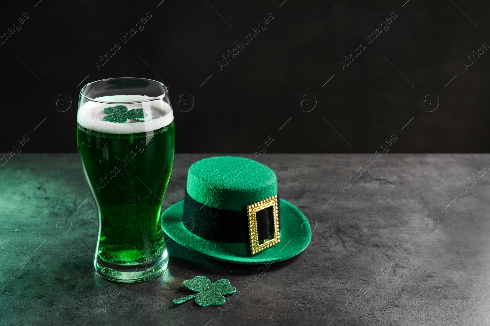 Photo of St. Patrick's day celebration. Green beer, leprechaun hat and decorative clover leaves on grey table. Space for text