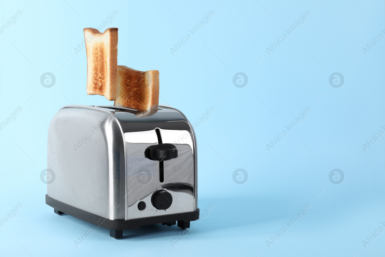 Photo of Bread slices popping up from modern toaster on light blue background. Space for text