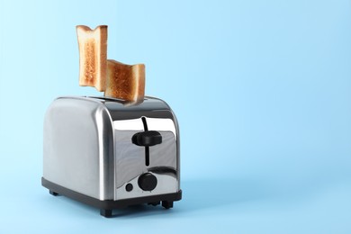 Photo of Bread slices popping up from modern toaster on light blue background. Space for text