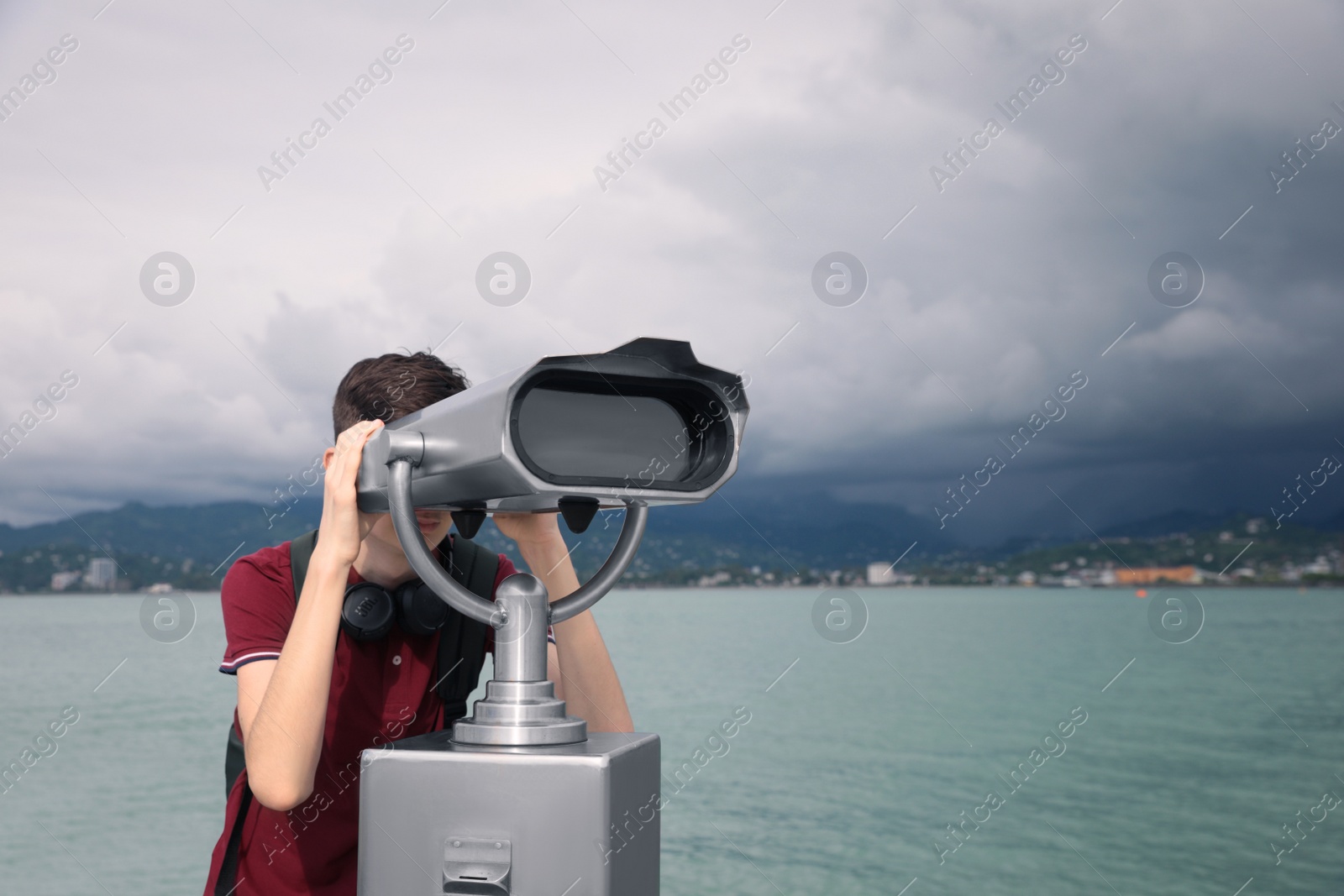 Photo of Teenage boy looking through mounted binoculars near sea. Space for text