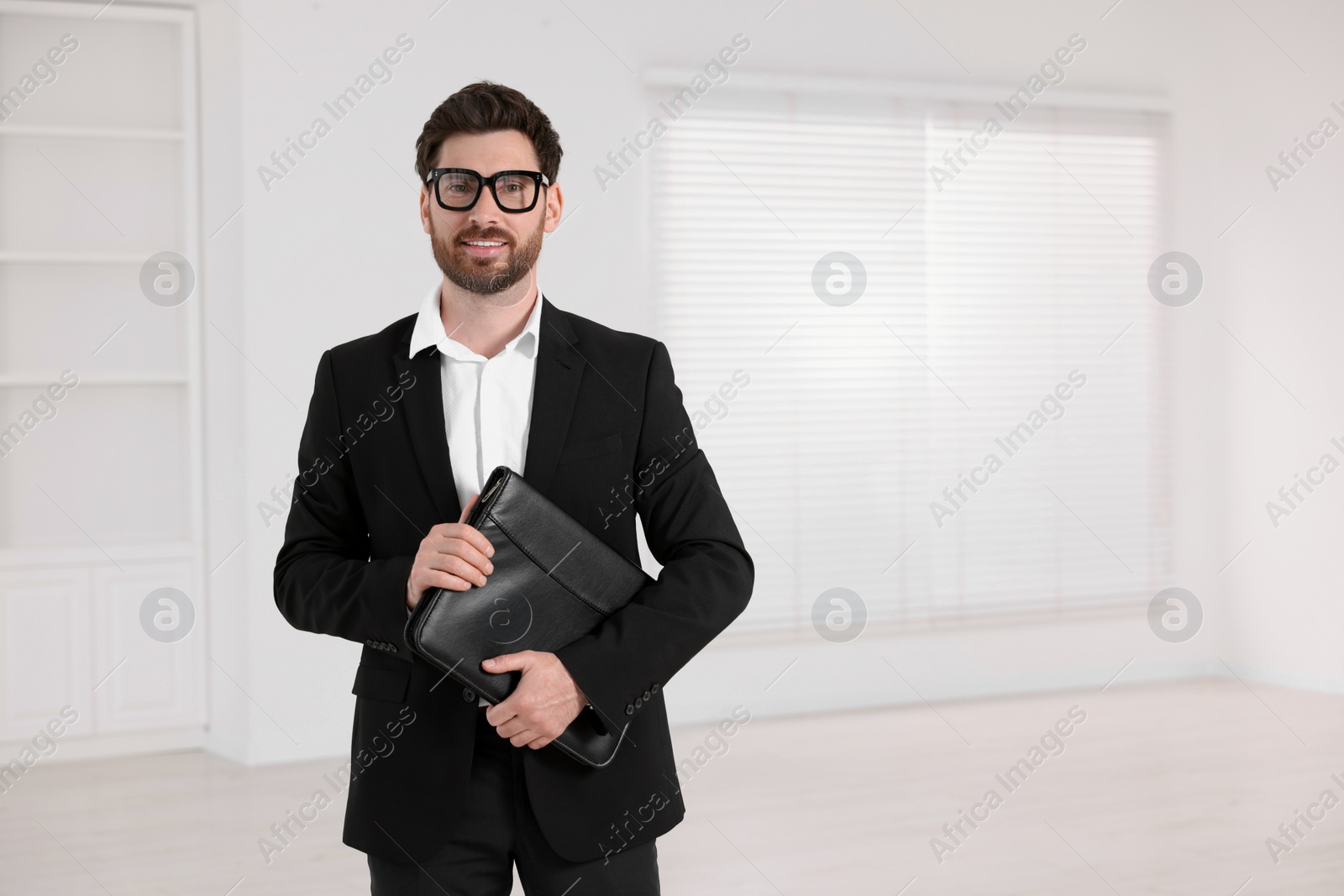 Photo of Happy real estate agent with leather portfolio indoors. Space for text