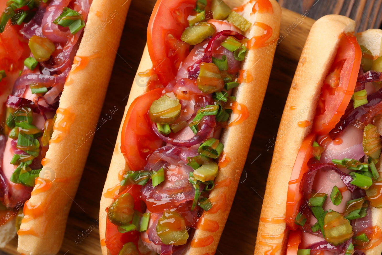 Photo of Tasty hot dogs with green onion, tomato, pickles and sauce on wooden table, above view