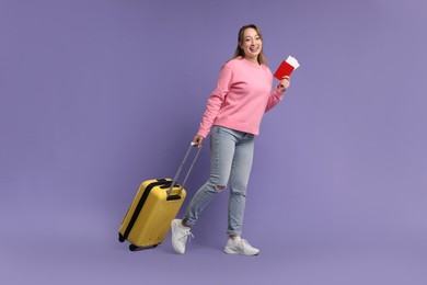 Photo of Happy young woman with passport, ticket and suitcase on purple background