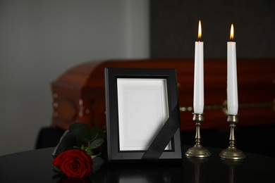 Photo of Black photo frame with burning candles and red rose on table in funeral home