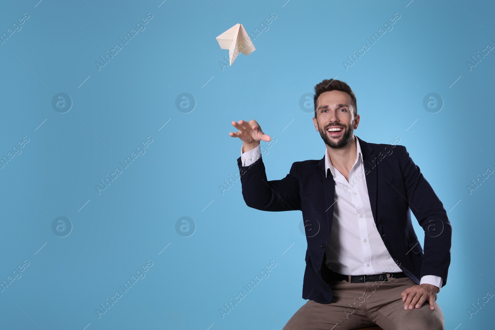 Photo of Handsome businessman playing with paper plane on light blue background. Space for text