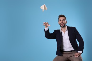 Handsome businessman playing with paper plane on light blue background. Space for text