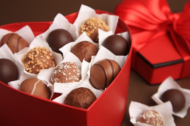 Heart shaped box with delicious chocolate candies on brown background, closeup