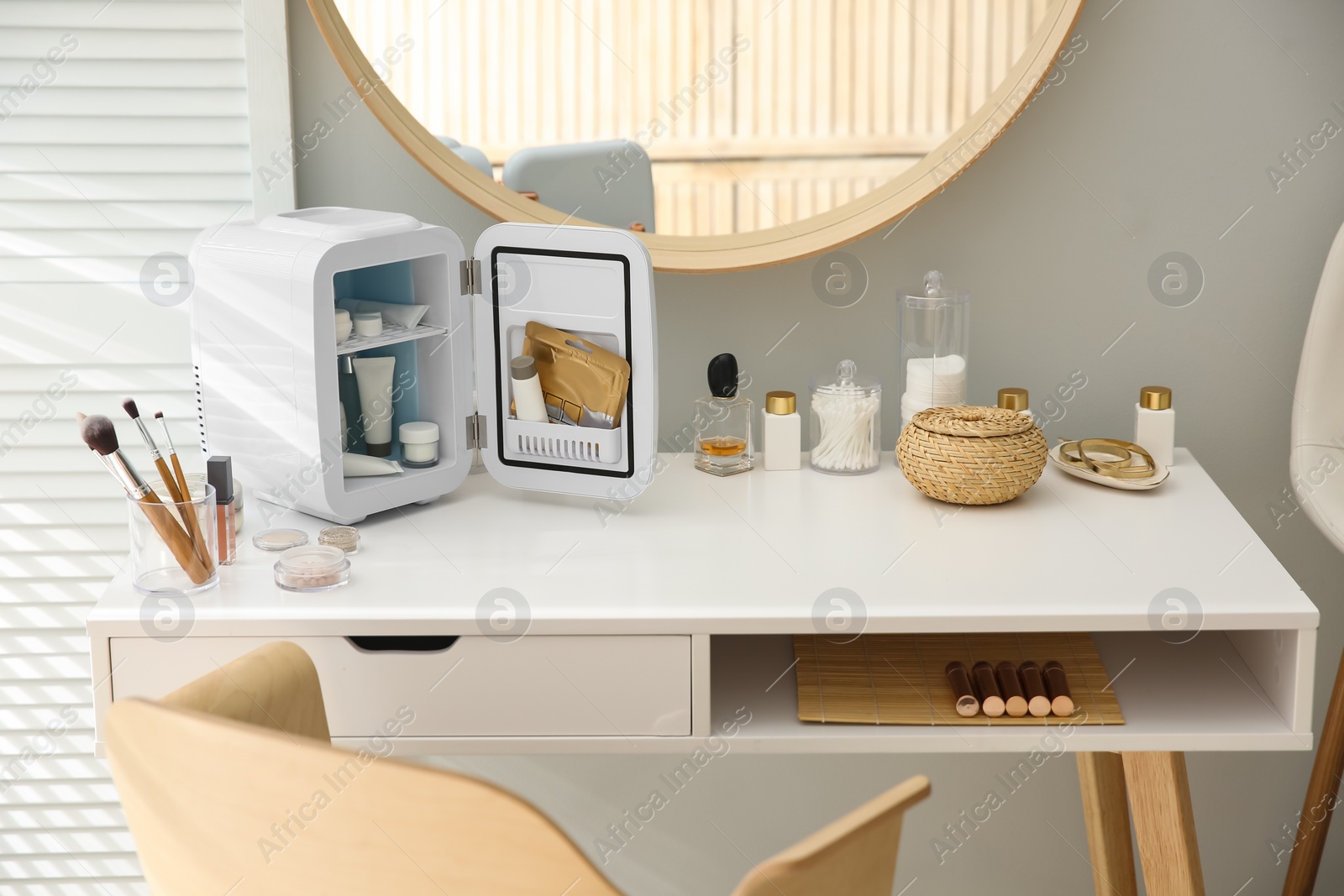 Photo of Cosmetics refrigerator and skin care products on white vanity table indoors