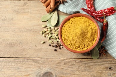 Photo of Curry powder in bowl and other spices on wooden table, flat lay. Space for text