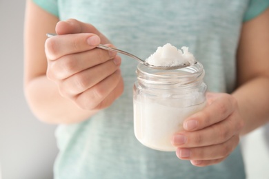 Photo of Woman holding jar and spoon with coconut oil, closeup. Healthy cooking