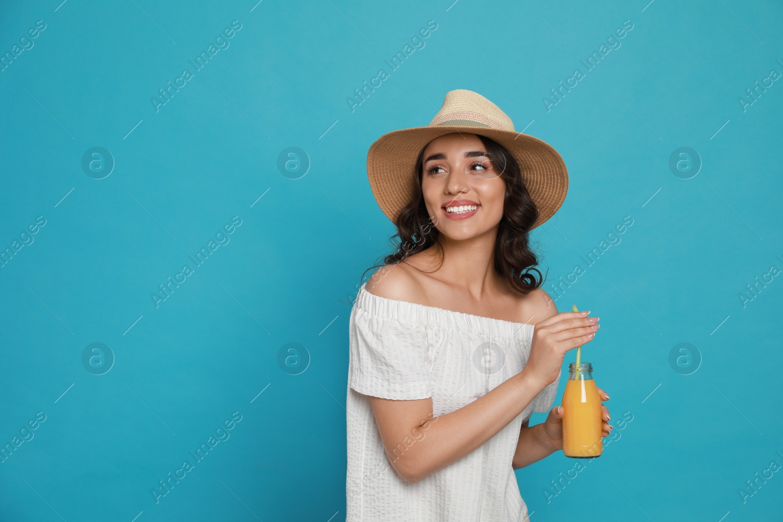 Photo of Beautiful young woman with straw hat and bottle of refreshing drink on light blue background. Space for text