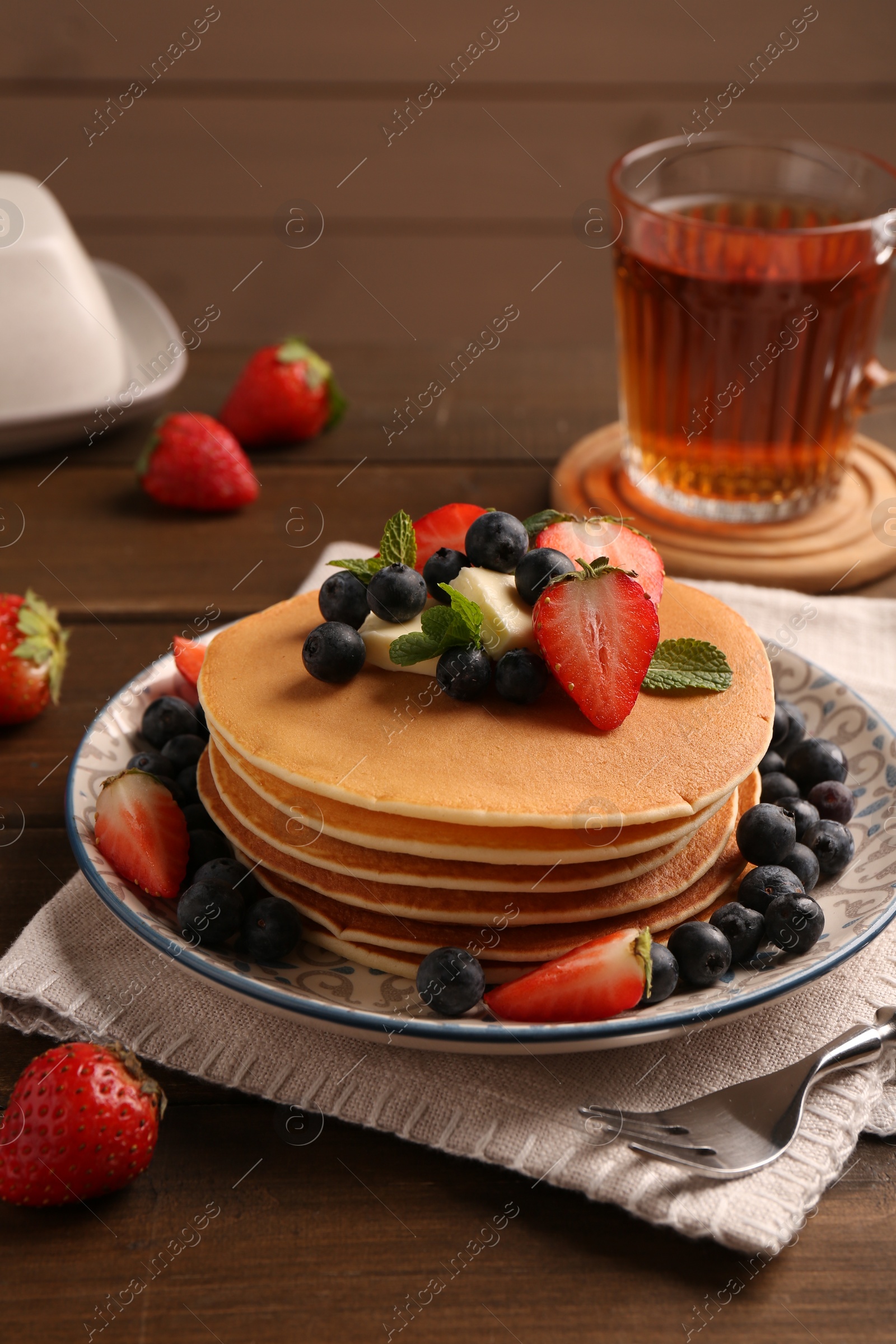 Photo of Delicious pancakes with fresh berries and butter served on wooden table
