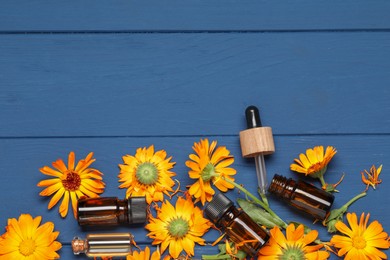 Bottles of essential oils and beautiful calendula flowers on blue wooden table, flat lay. Space for text