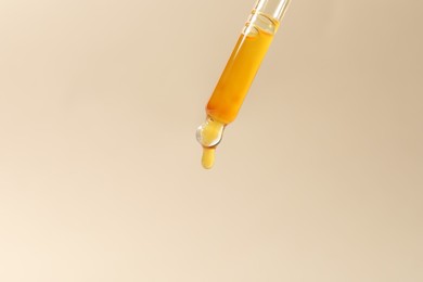 Dripping cosmetic serum from pipette on beige background, closeup