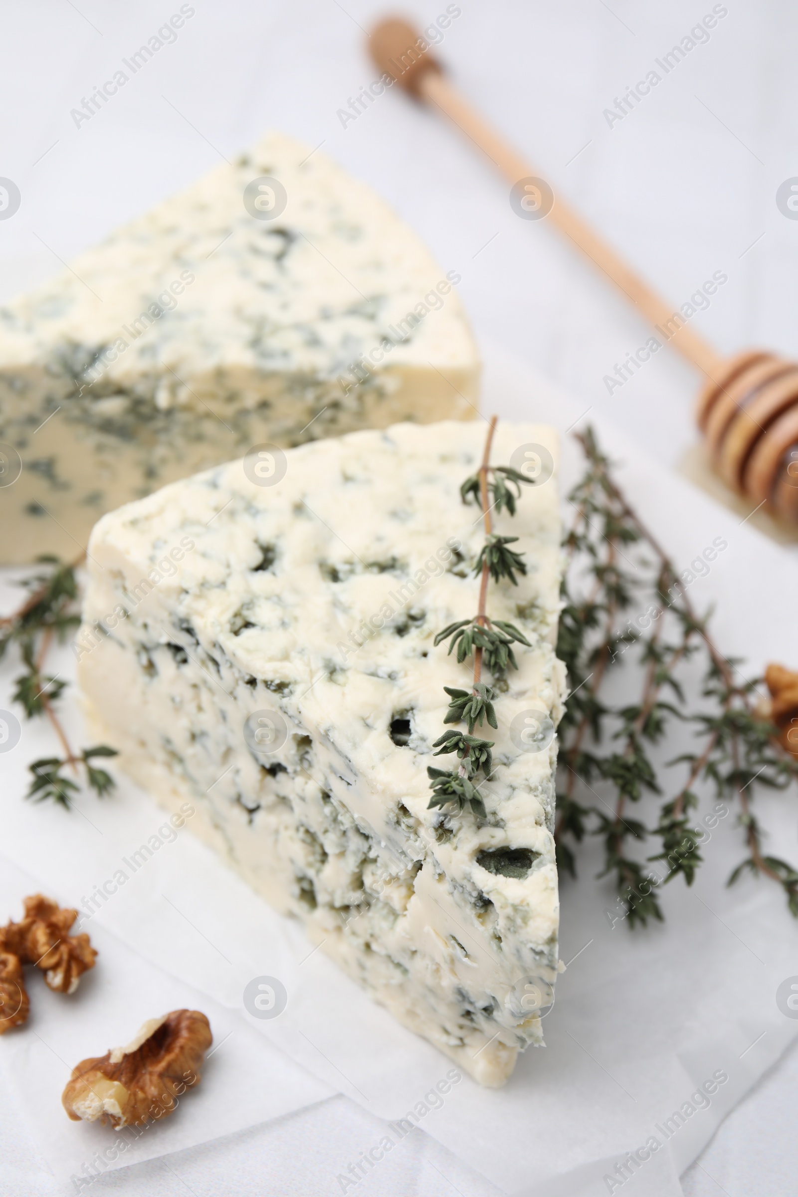 Photo of Tasty blue cheese with thyme, walnuts and honey dipper on white table, closeup