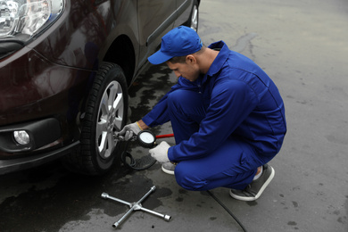 Worker checking tire pressure in car wheel at service station